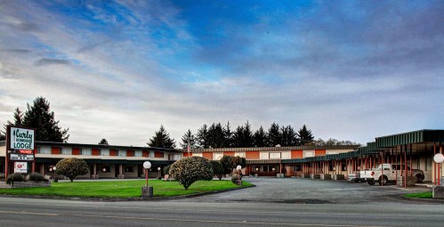 A roadside motel with a sign, surrounded by green lawns and trees under a cloudy sky.