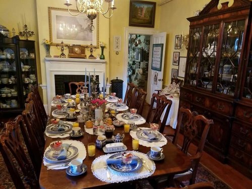 A beautifully set dining table with fine china, candles, and flowers, surrounded by elegant furniture in a warm room.
