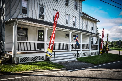 A white multi-story building with banners and flags outside, located near a road with green grass in front.