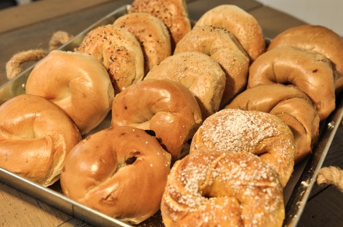 A tray of assorted bagels, including plain, sesame, and cinnamon varieties, arranged neatly on a wooden surface.