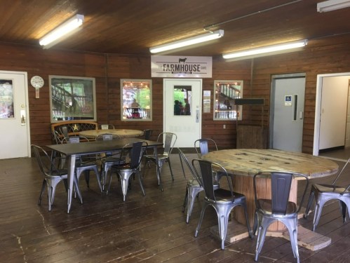 Interior of a rustic farmhouse dining area with wooden floors, round and rectangular tables, and a welcoming atmosphere.