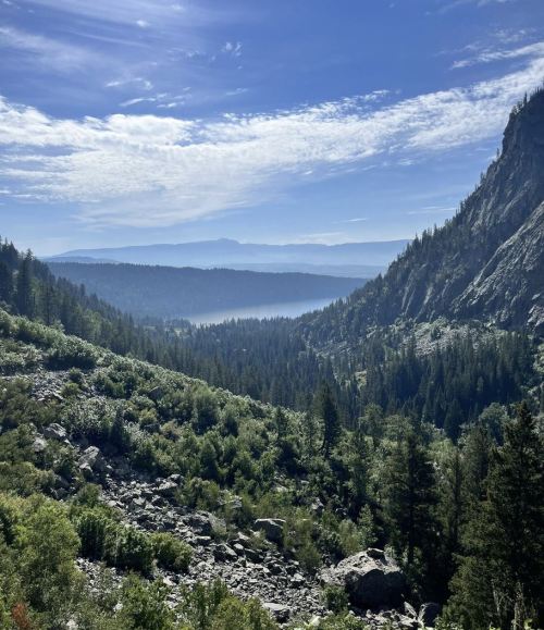 A scenic view of a mountainous landscape with lush greenery, rocky terrain, and a blue sky with wispy clouds.