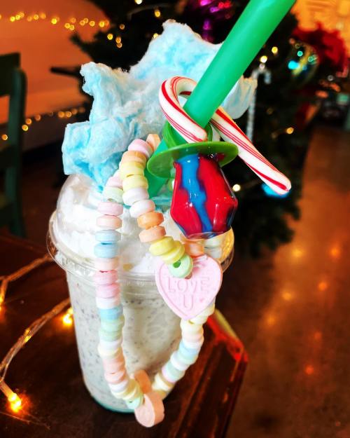 A colorful milkshake topped with cotton candy, a candy cane, and a necklace of pastel candy hearts.
