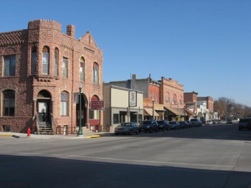 A quiet street lined with historic brick buildings and parked cars under a clear blue sky.
