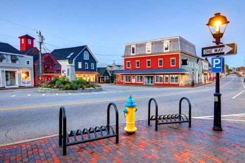 A quaint town square at dusk, featuring colorful buildings, a fire hydrant, and a lamp post with a one-way sign.