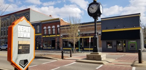 A street view of Depot Town featuring historic buildings, a clock tower, and a sign marking the area.