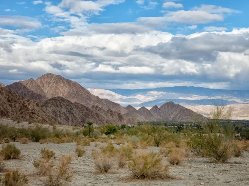 A scenic view of rugged mountains under a cloudy sky, with sparse vegetation in the foreground.