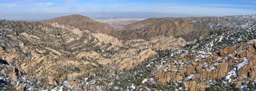 A panoramic view of rugged mountains and valleys, with snow-capped peaks and a clear blue sky above.