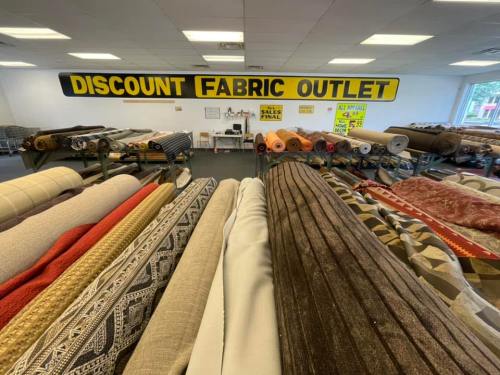 Interior of a fabric store with rolls of fabric on display and a large sign reading "DISCOUNT FABRIC OUTLET."