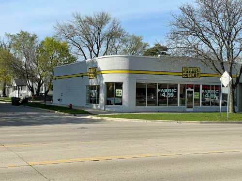 A fabric outlet store with large windows displaying a sign for fabric priced at $4.99, located on a street corner.