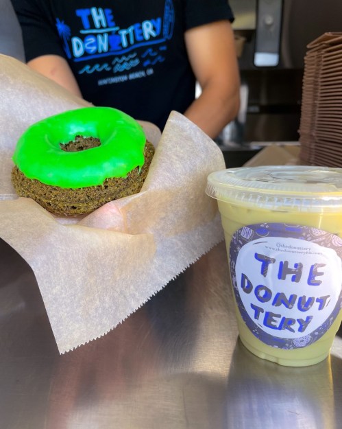 A green donut on parchment paper next to a cup labeled "THE DONUTERY" filled with a yellow beverage.