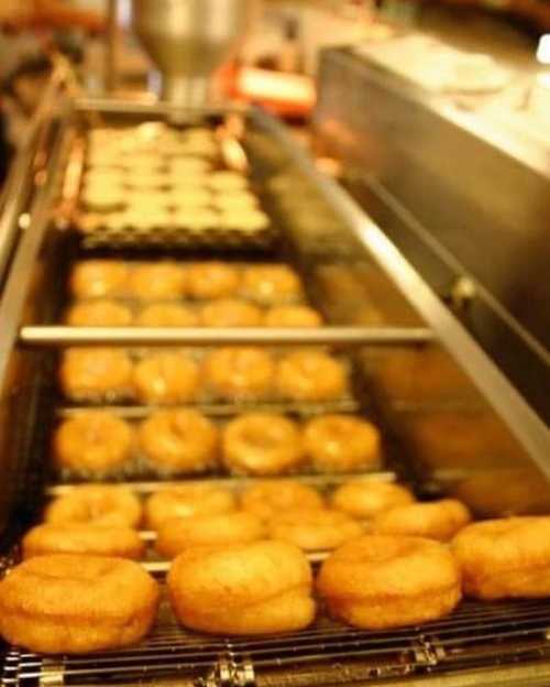 A fryer filled with golden-brown donuts cooking, with some donuts on a rack above.