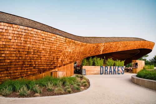 A modern wooden building with a curved roof, featuring the name "Drake's" prominently displayed at the entrance.