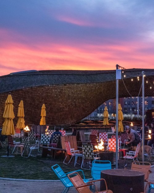 A vibrant sunset over a cozy outdoor seating area with colorful chairs and fire pits.