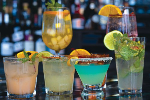 A variety of colorful cocktails with garnishes, displayed on a bar counter.