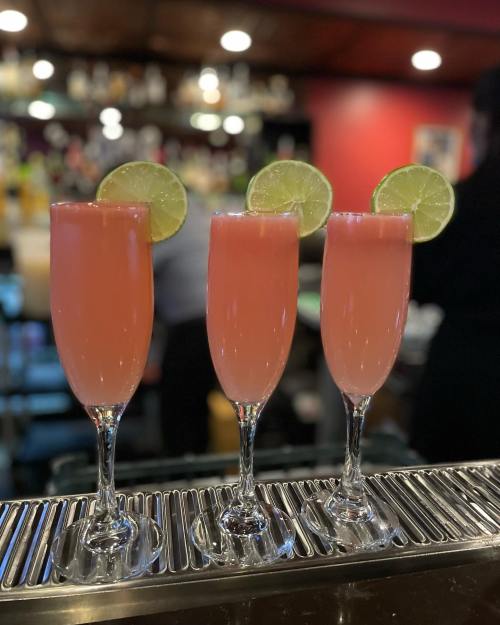 Three pink cocktails with lime slices on the rim, displayed on a bar counter.