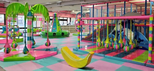 Brightly colored indoor play area with climbing structures, swings, and soft play equipment. Fun and vibrant atmosphere.