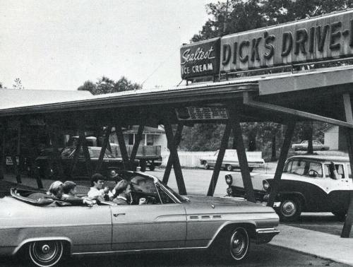 A vintage black-and-white photo of a convertible car at a drive-in restaurant with a sign for ice cream.