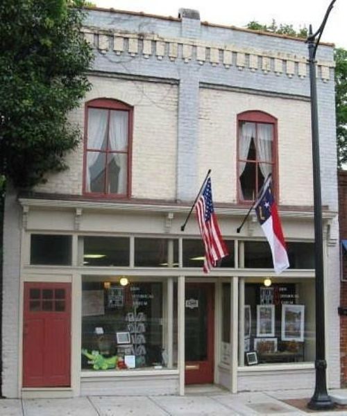 Historic two-story building with red accents, large windows, and American and state flags displayed outside.