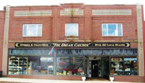 A brick storefront featuring "The Dream Catcher" sign, showcasing antiques and collectibles with large display windows.