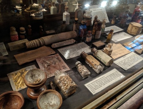 A display case filled with various vintage bottles, jars, and artifacts, alongside informational cards.