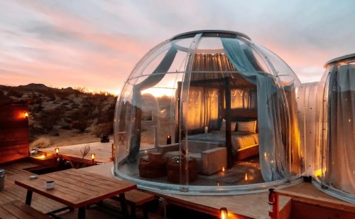 A transparent bubble hotel room at sunset, surrounded by desert landscape and softly glowing lanterns.