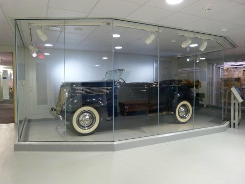 A vintage convertible car displayed in a glass case in a museum setting.