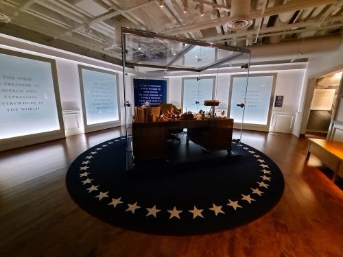 A modern exhibit featuring a central desk surrounded by illuminated walls with text and a star-patterned floor.