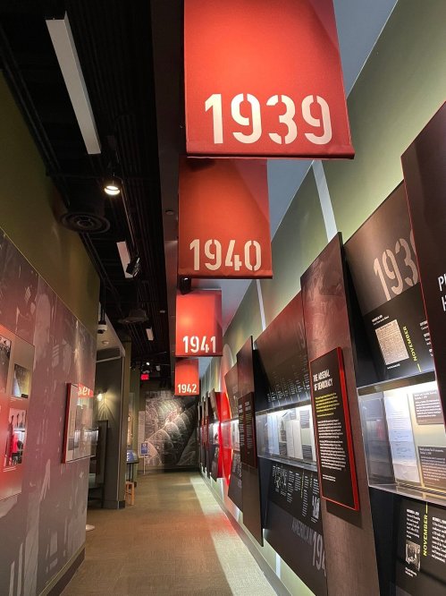 A museum hallway featuring hanging banners with the years 1939, 1940, 1941, and 1942, alongside informational displays.