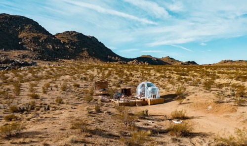 A dome-shaped structure in a desert landscape, surrounded by sparse vegetation and rocky hills under a blue sky.