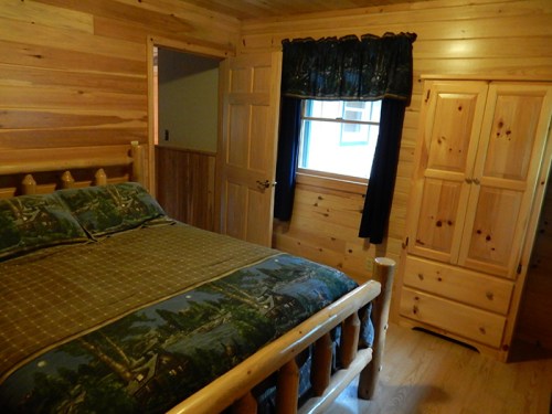 Cozy wooden bedroom with a log bed, patterned bedding, and a wardrobe, featuring warm wood paneling and a window.
