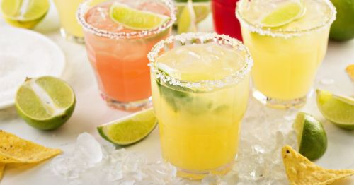 Colorful cocktails with lime slices, garnished with salt, surrounded by lime wedges and tortilla chips on ice.