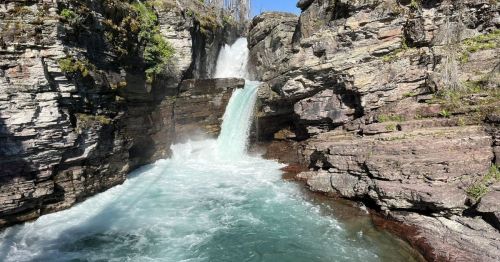 A waterfall cascading over rocky cliffs into a turquoise pool, surrounded by lush greenery and clear blue skies.