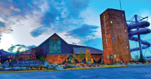 Exterior view of Fairmont Hot Springs Resort, featuring a modern building and a water slide against a colorful sky.
