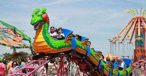 Children enjoy a colorful dragon-themed roller coaster at a lively amusement park.