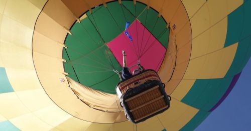 A colorful hot air balloon viewed from below, with a basket and a person waving from inside.