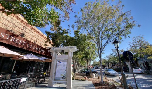 A sunny street scene featuring a restaurant, trees, and a signpost in a lively outdoor area.