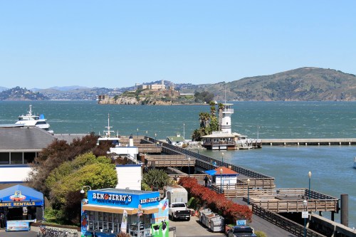 View of a waterfront with boats, a pier, and Alcatraz Island in the background under a clear blue sky.