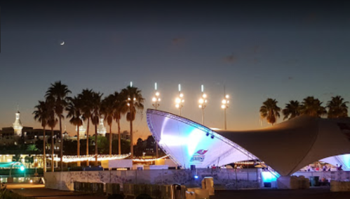 A nighttime view of a venue with palm trees, lights, and a crescent moon in the sky.