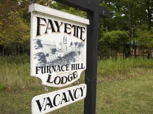 Sign for Fayette Furnace Hill Lodge with "Vacancy" displayed, surrounded by trees and greenery.