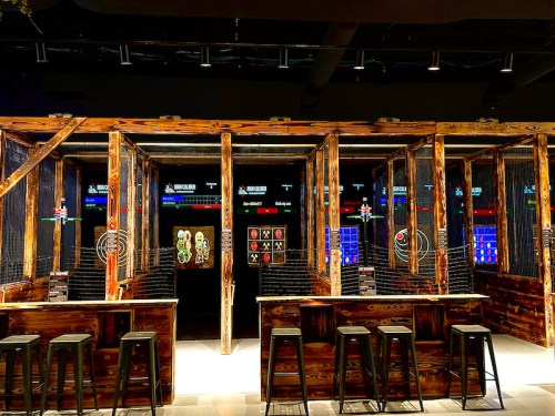 A modern gaming venue with wooden structures, bar seating, and digital screens displaying various games.
