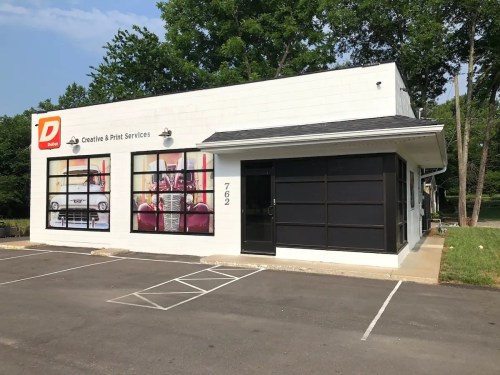 A white building with a black roof and large windows, featuring signage for "Creative & Print Services."