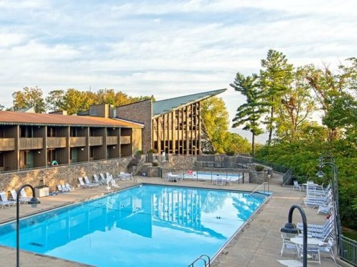 A scenic view of a hotel pool area surrounded by trees and a modern building with a sloped roof.
