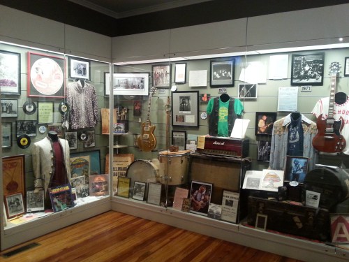 Display case featuring vintage music memorabilia, including instruments, records, photos, and concert posters.