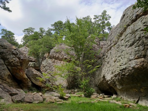 A rocky landscape with large boulders and green trees under a partly cloudy sky.