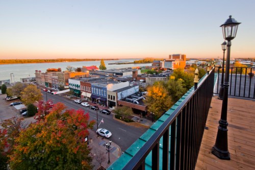 A scenic view of a riverside town at sunset, showcasing colorful trees and historic buildings along the waterfront.
