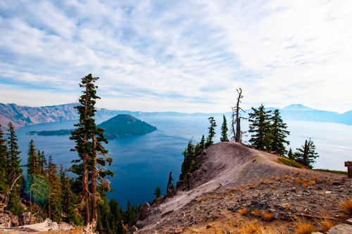 A scenic view of Crater Lake, featuring an island surrounded by trees and a blue sky with scattered clouds.