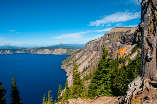 A scenic view of Crater Lake, surrounded by steep cliffs and lush green trees under a clear blue sky.