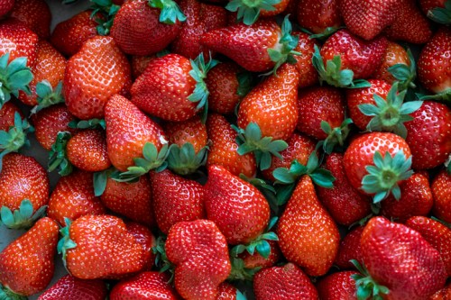 A close-up of fresh, ripe strawberries with vibrant red color and green leaves scattered across the surface.