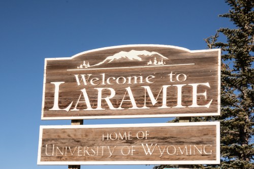 Wooden sign welcoming visitors to Laramie, home of the University of Wyoming, with mountains in the background.